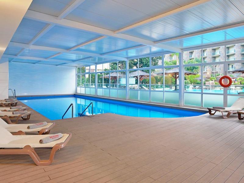 Vnitřní bazén s několika lehátky a velkými okny s výhledem na venkovní prostor.