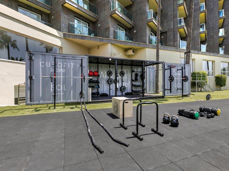 Venkovní fitness prostor před hotelem s posilovacími zařízeními a bradly.