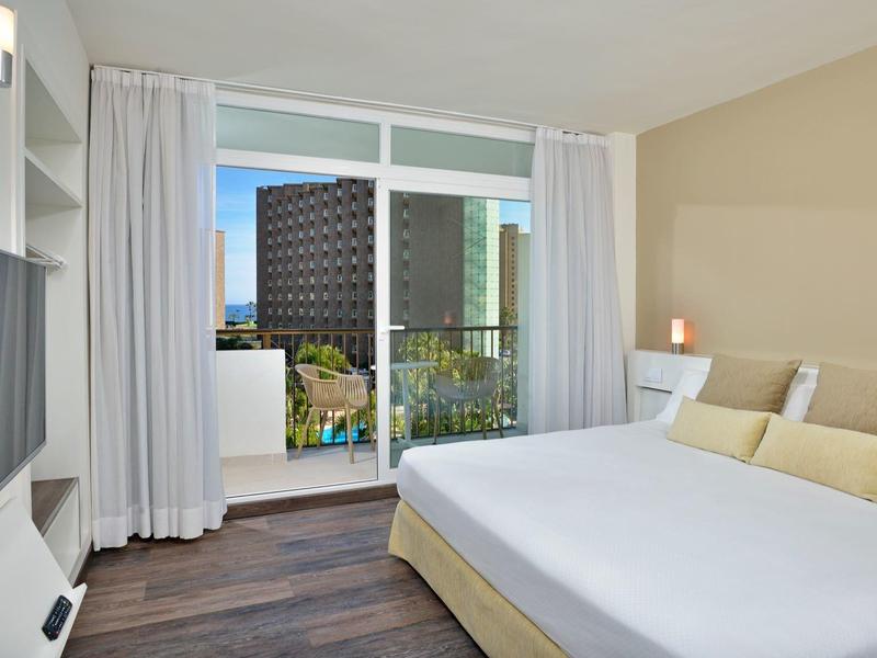 Světý hotelový pokoj s velkou postelí, TV a balkonem s výhledem na město.