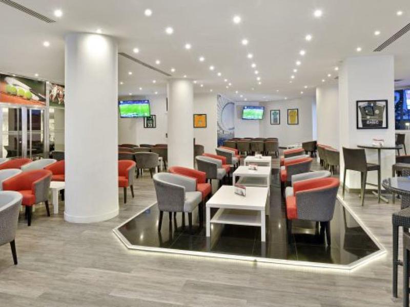 Moderní hotelový salonek se šedými a červenými křesly a jasným osvětlením.