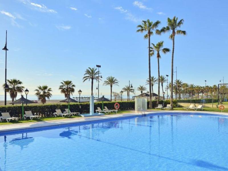 Modrý bazén s lehátky, palmami a modrou oblohou u moře.