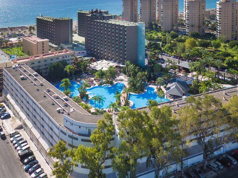 Velký hotel s několika bazény obklopený zelení s výhledem na moře.