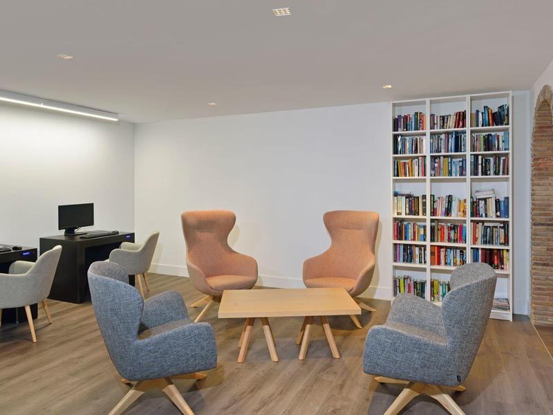 Gemütlicher Sitzbereich mit Sesseln, Holzfußboden, Bücherregal und Arbeitsplatz mit Computern.