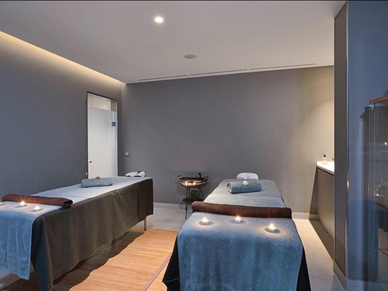 Moderner Behandlungsraum mit zwei Massageliegen, gedämpfter Beleuchtung und beruhigender Atmosphäre.