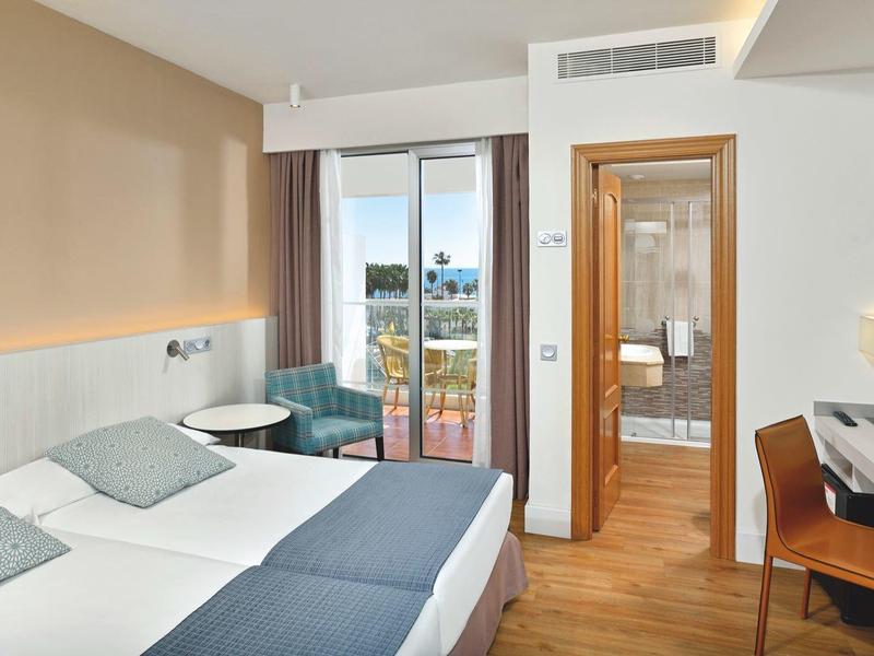 Helles, modernes Schlafzimmer mit Doppelbett, Holzboden, Balkon und angrenzendem Bad.