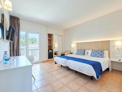 Světý hotelový pokoj se dvěma postelemi, modrými akcenty, dlažbou a dveřmi na balkon.