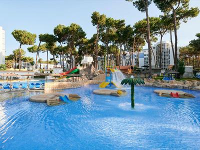 Venkovní bazén s tobogány, vodními atrakcemi a lehátky obklopený stromy.