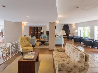 Prostorný hotelový salonek s béžovými pohovkami, křesly a velkými okny vpouštějícími přirozené světlo.