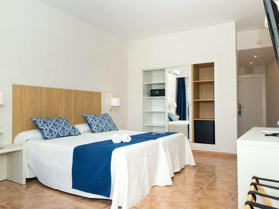 Světlý hotelový pokoj se dvěma lůžky, modro-bílým povlečením a dřevěným nábytkem.