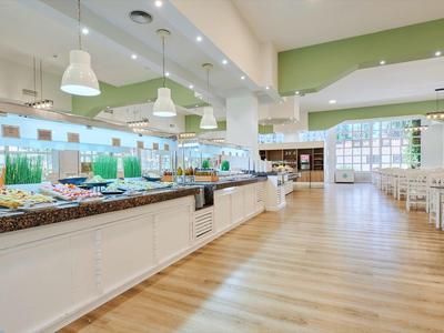 Světlá bufetová část hotelu s salátovým barem a dřevěnou podlahou pod bílým stropním osvětlením.