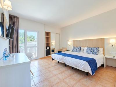 Helles Hotelzimmer mit Doppelbett, Schreibtisch, Schrank und Balkontür mit Blick ins Freie.