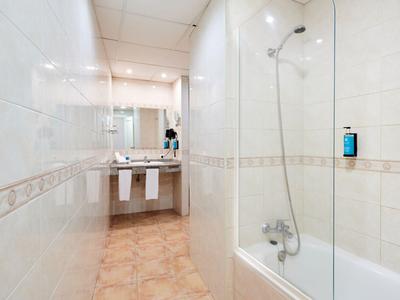 Helles Badezimmer mit weißer Fliesenwand, Badewanne und Waschbecken unter großem Spiegel.