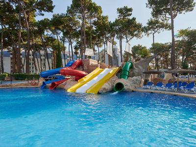 Hellblauer Pool mit bunten Wasserrutschen und Liegebereichen unter Bäumen.