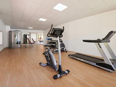 Moderner Fitnessraum mit Laufband, Heimtrainer und Gewichten in hellem, geräumigem Raum.