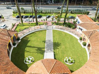 Pohled na kruhovou zahradu se zelenou trávou a cestičkami, obklopenou budovami s terakotovými střechami.