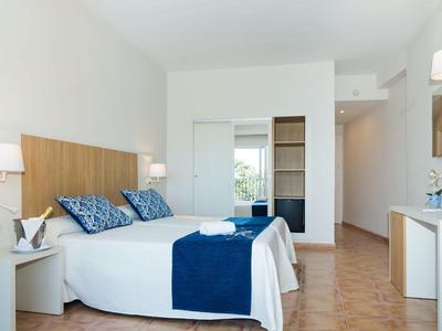 Moderní hotelový pokoj s manželskou postelí, modrými doplňky, nástěnnými lampami, TV a malou ledničkou.