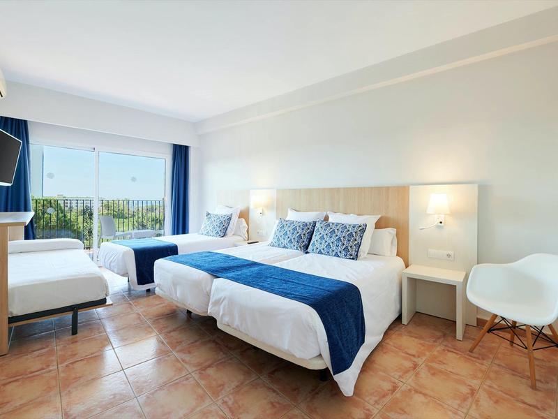 Moderní hotelový pokoj se dvěma postelemi, modrými akcenty, televizí a balkonem s výhledem.