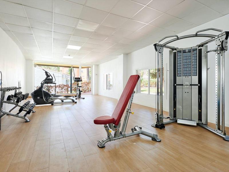 Světle hotelové fitness s moderním vybavením a velkými okny pro přirozené světlo.