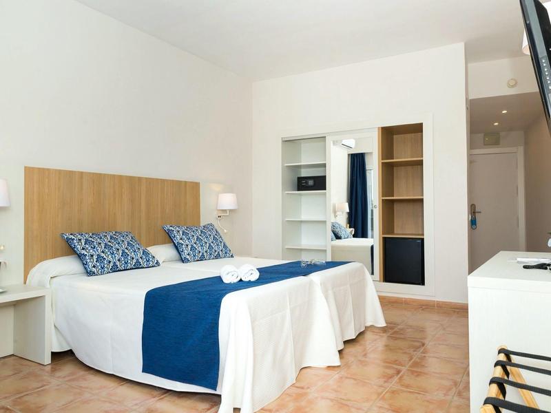 Světlý hotelový pokoj se dvěma lůžky, modro-bílým povlečením a dřevěným nábytkem.