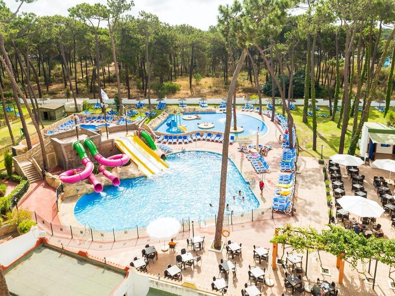 Venkovní vodní park s tobogány, bazénem, lehátky a okolními stromy.