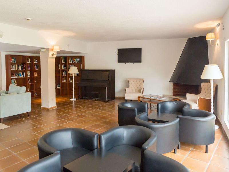 Světlý salonek s černými křesly, pianem a televizí na zdi.