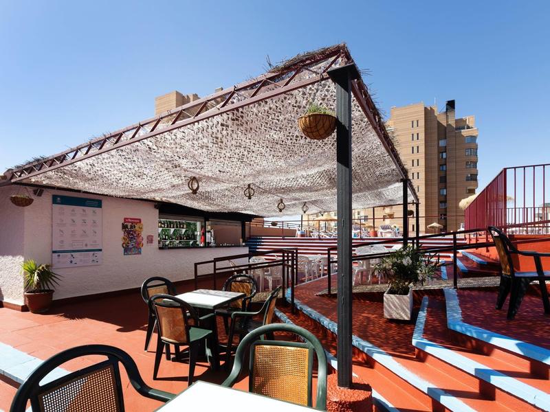 Terrazza sul tetto con sedie, tavoli e copertura solare sotto un cielo sereno.