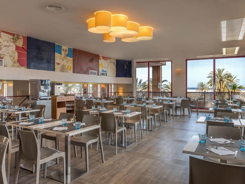 Ristorante moderno con molti tavoli, sedie e una grande finestra con vista sulle palme.