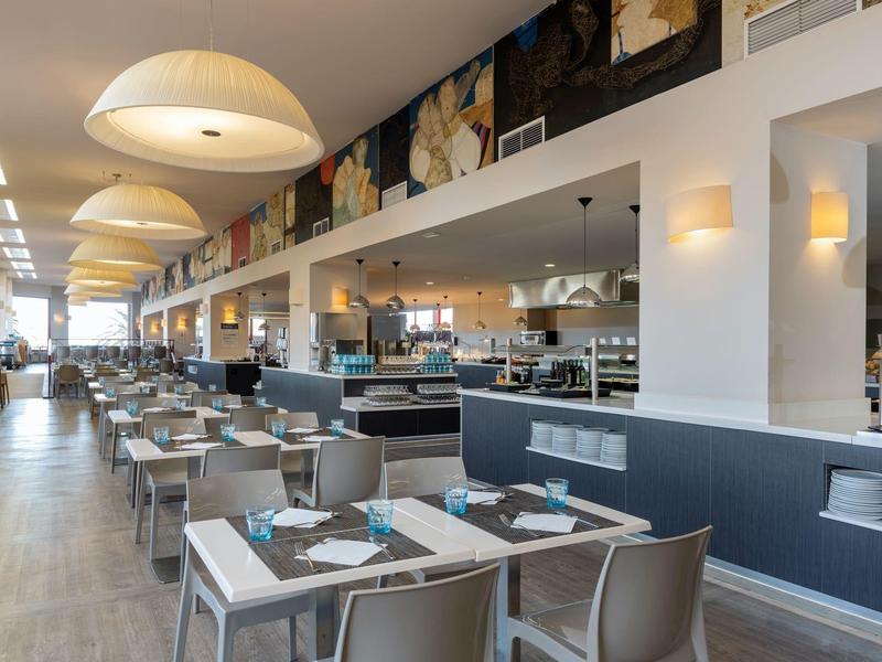 Ampia sala da pranzo moderna con tavoli bianchi e sedie grigie in ambiente luminoso.