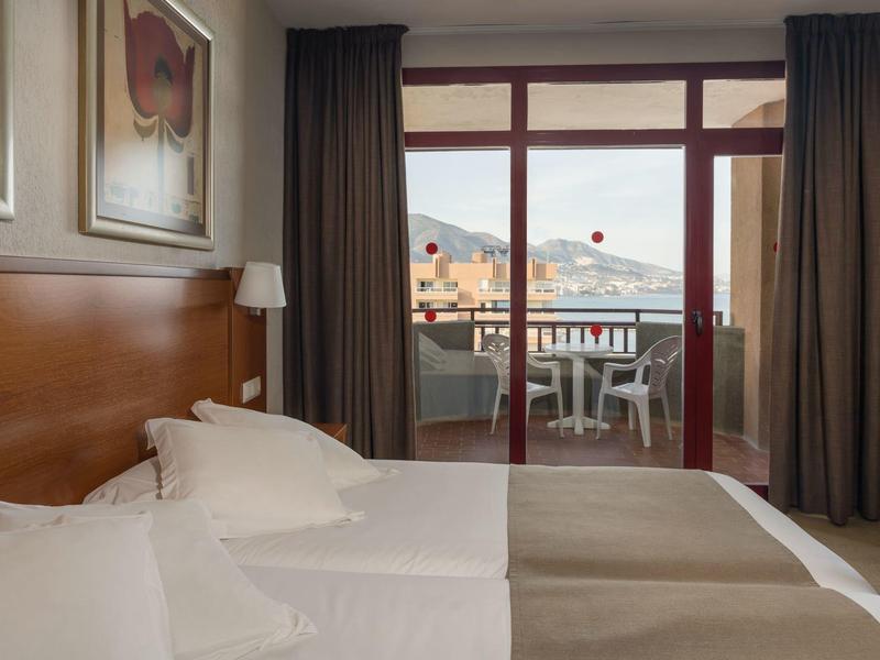 Camera d'hotel con due letti e accesso a una terrazza con vista sulle montagne.