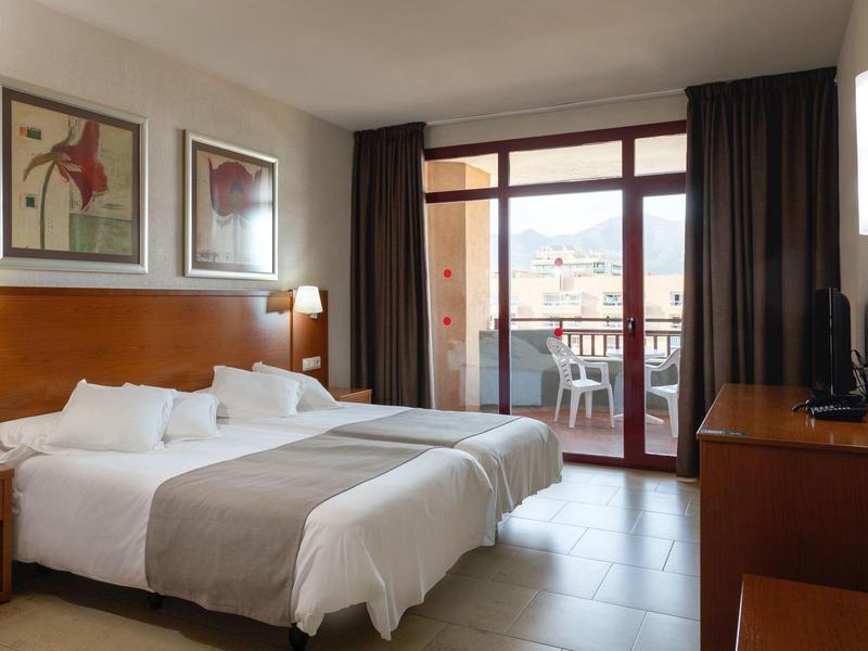 Camera d'hotel luminosa con due letti, balcone e vista sulla città.