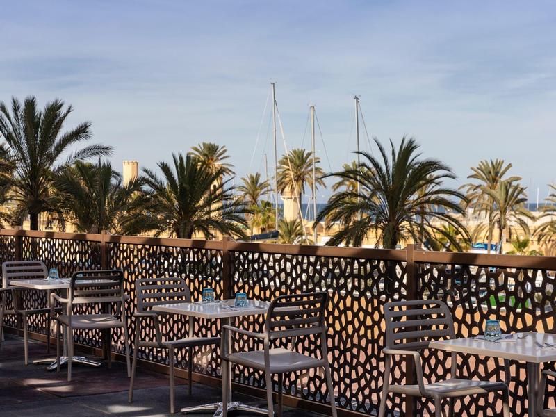 Terrazza con sedie e tavoli, circondata da palme sotto un cielo sereno.