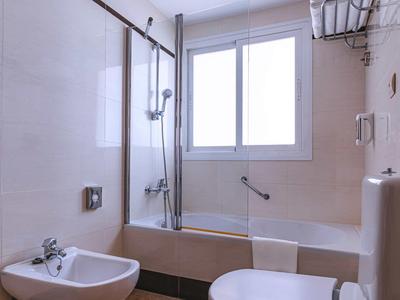 Bright bathroom with bathtub, shower screen, bidet, and toilet under a large window.