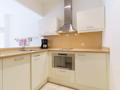 Modern kitchenette with stove, oven, extractor hood, and coffee maker in a light design.