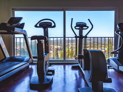 Fitnessraum mit Laufband und Trainingsgeräten vor großen Fenstern mit Aussicht.