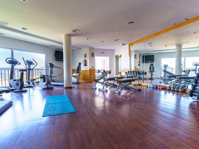 Heller Fitnessraum mit Hartholzboden und modernen Trainingsgeräten neben großen Fenstern.