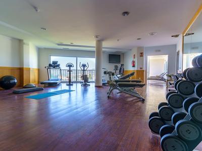 Geräumiger Fitnessraum mit Hanteln, Trainingsgeräten und Yogamatten auf Holzboden.