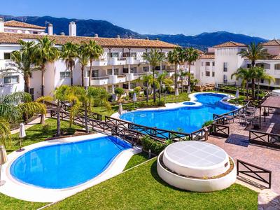 Hotel complex with multiple pools, bridges, and palm trees against a mountainous backdrop and clear sky.
