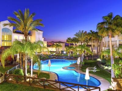 Evening shot of a lit pool surrounded by tropical gardens and hotel buildings.