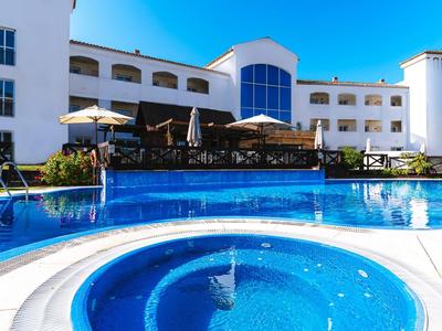Modern hotel complex with large outdoor pool and jacuzzi under sunny weather