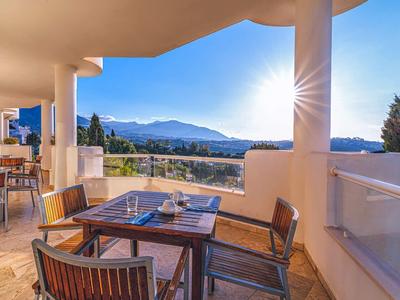Terrasse mit Holztisch und Stühlen, Panorama-Bergblick und hellblauem Himmel bei Sonnenlicht.