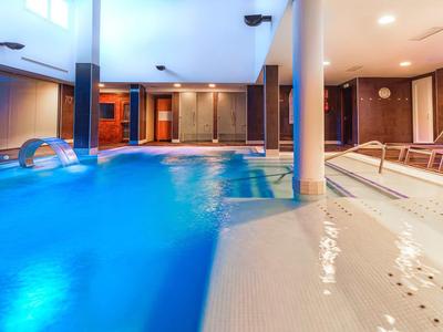 Modern indoor pool with lighting and lounge chairs in a hotel.