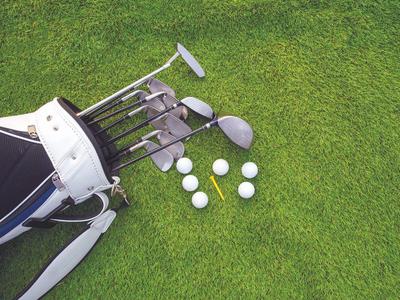 Golfbag mit Golfschlägern und Golfbällen auf grünem Rasen.