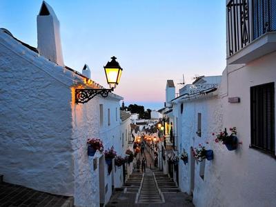 Evening alley in a picturesque village with white houses and flowers on the walls.