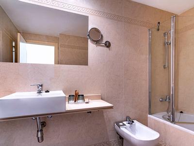 Modern bathroom with sink, wall mirror, bidet, and bathtub with shower partition.