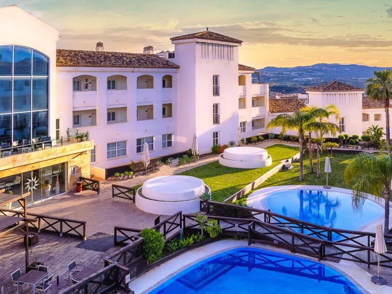 Luxury hotel with pools, green areas, and sea view at sunset.