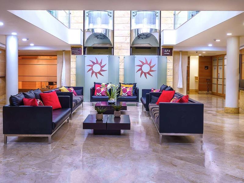 Modern hotel lobby with black sofas, red cushions, and glass coffee table on marble floor.