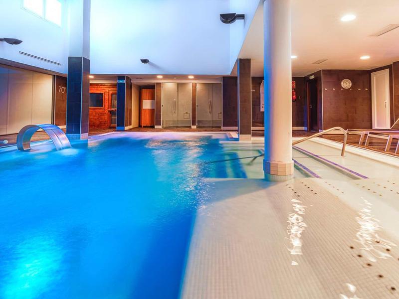 Modern indoor pool with lighting and lounge chairs in a hotel.