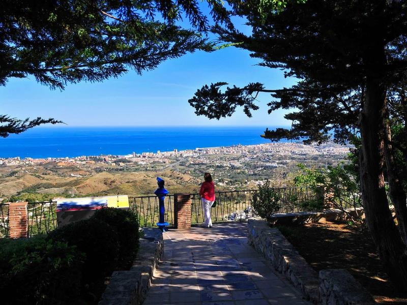 View from a shaded park overlooking the coastal town and blue sea in the background.