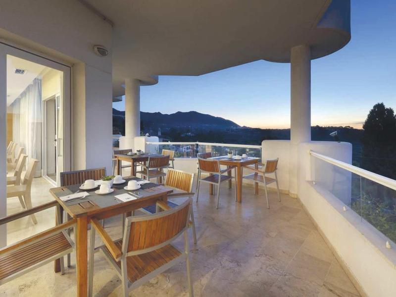 Spacious balcony with dining area and mountain view at sunset in a hotel.