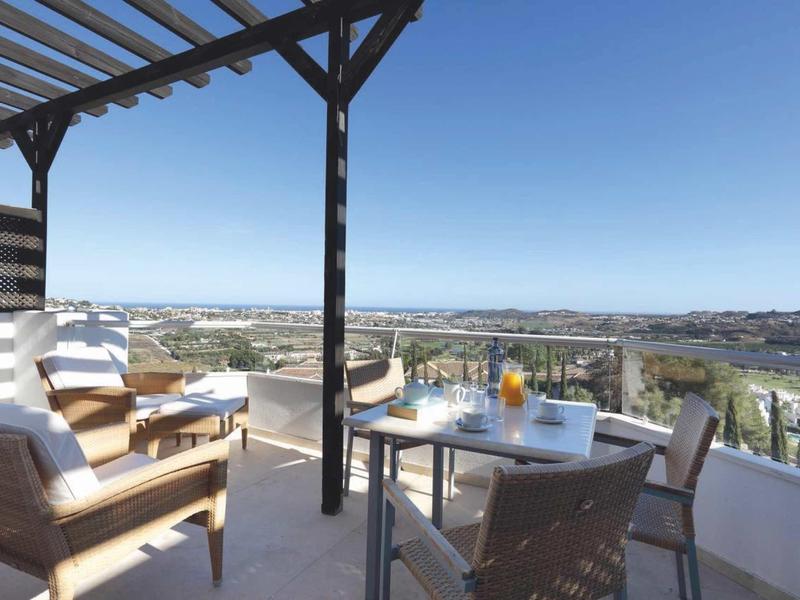 Balcony with seating and table with drinks, overlooking river and landscape.